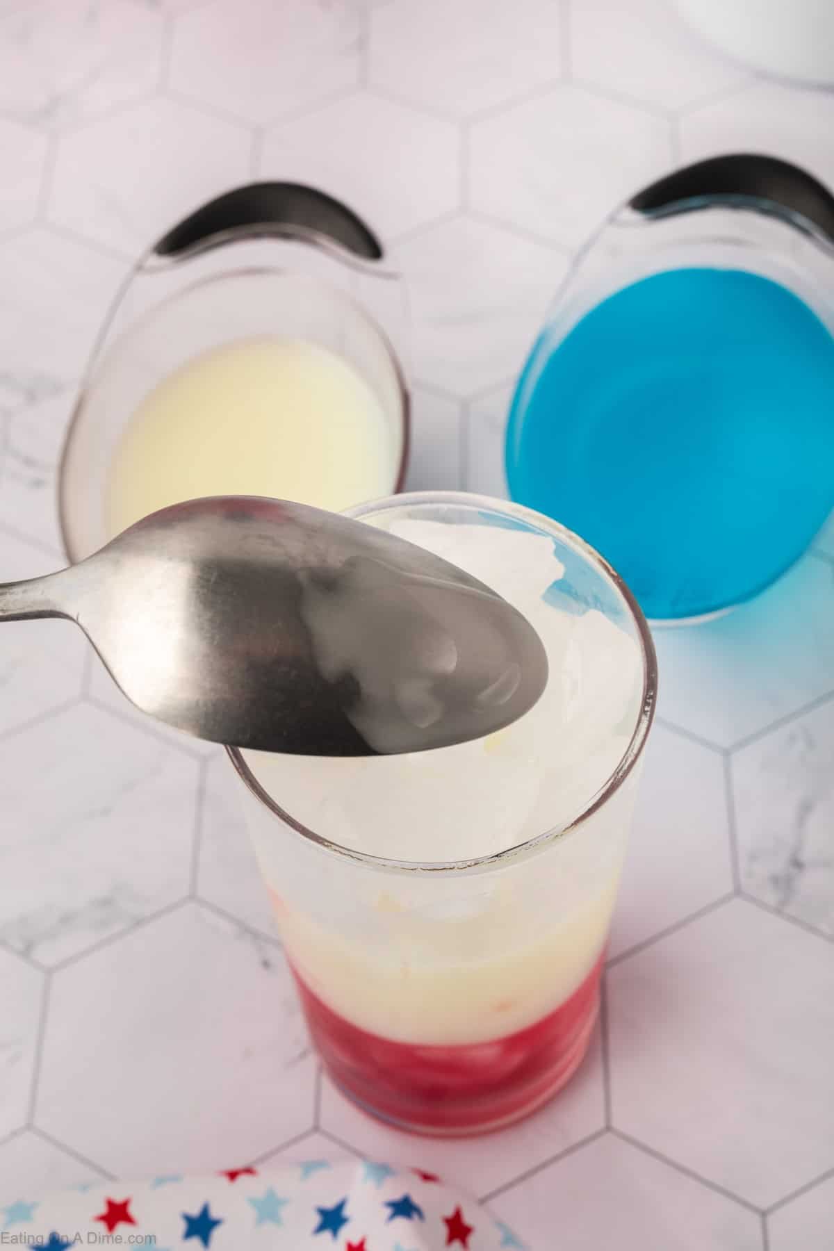 Pouring the Pina Colada in a glass with ice cubes on top of the red juice