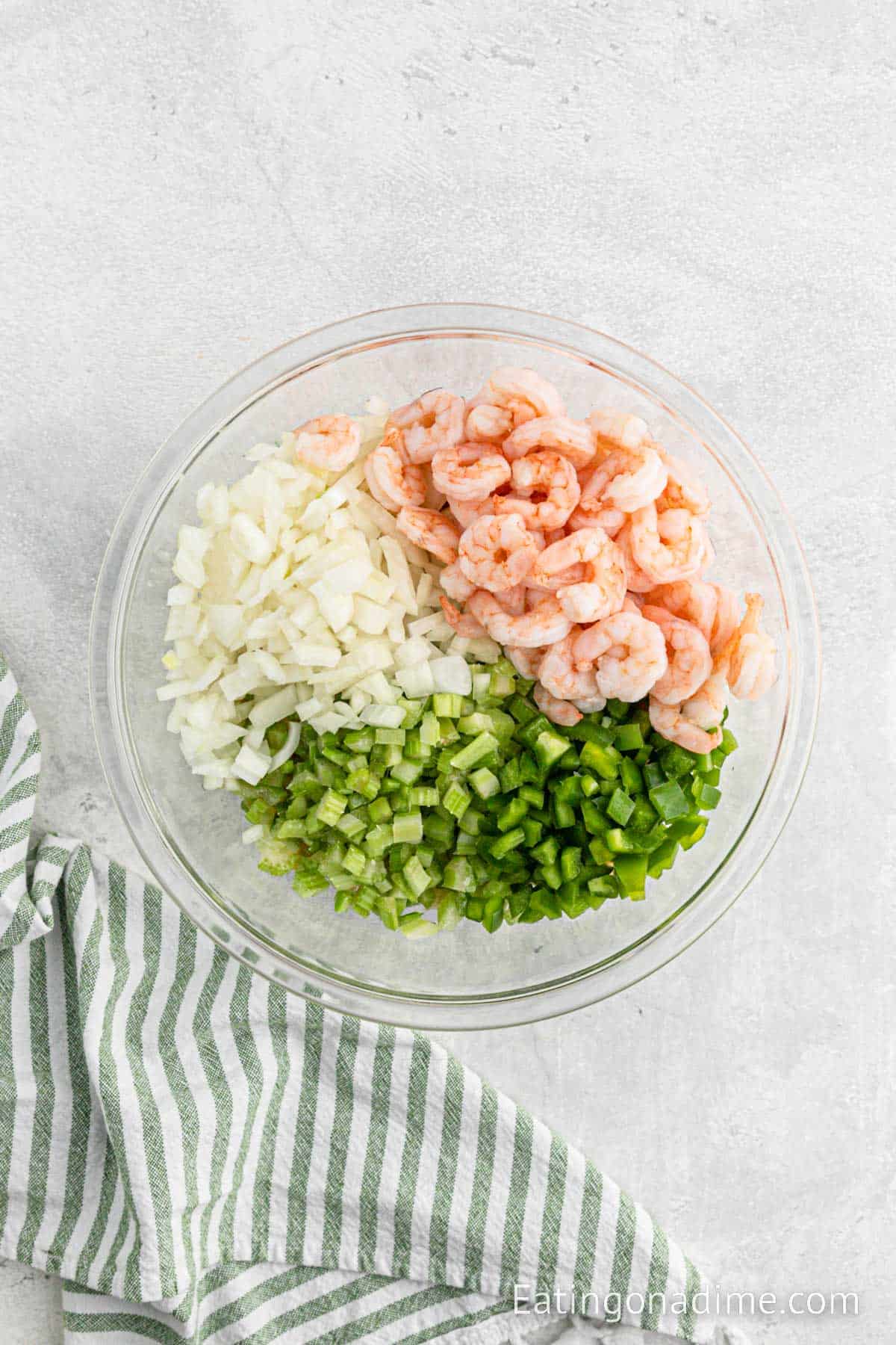 Chopped onions, cooked shrimp, chopped celery, and chopped green bell peppers in a bowl
