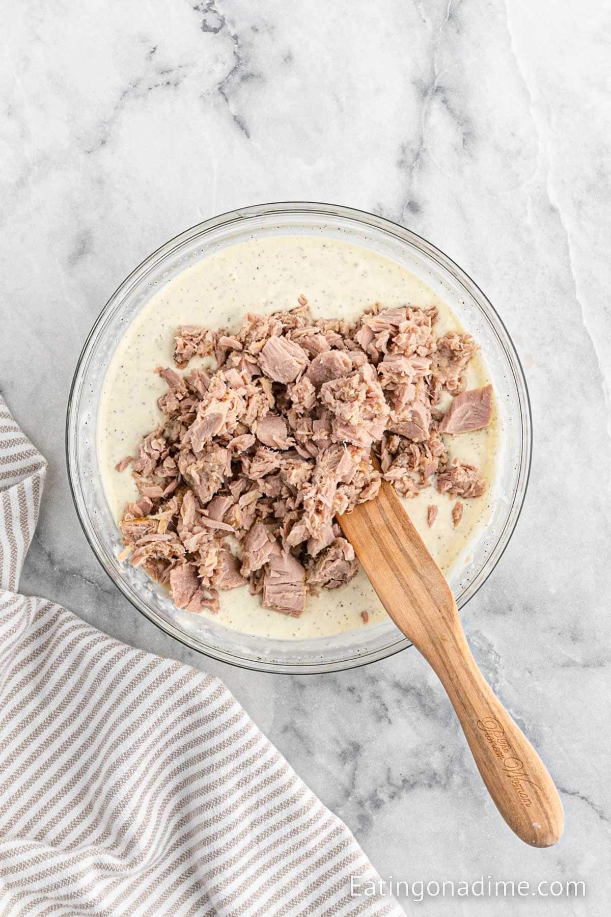 Mixing in the chopped tuna in the dressing mixture with a wooden spoon