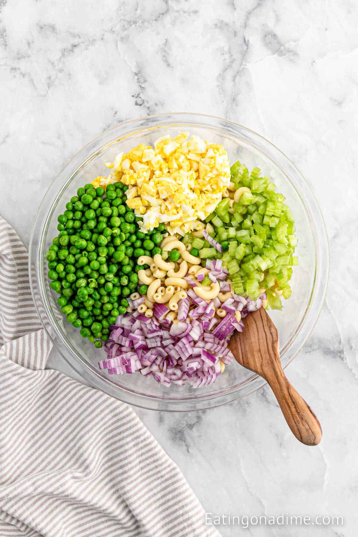 Peas, celery, onion, eggs and pasta in a bowl with a wooden spoon