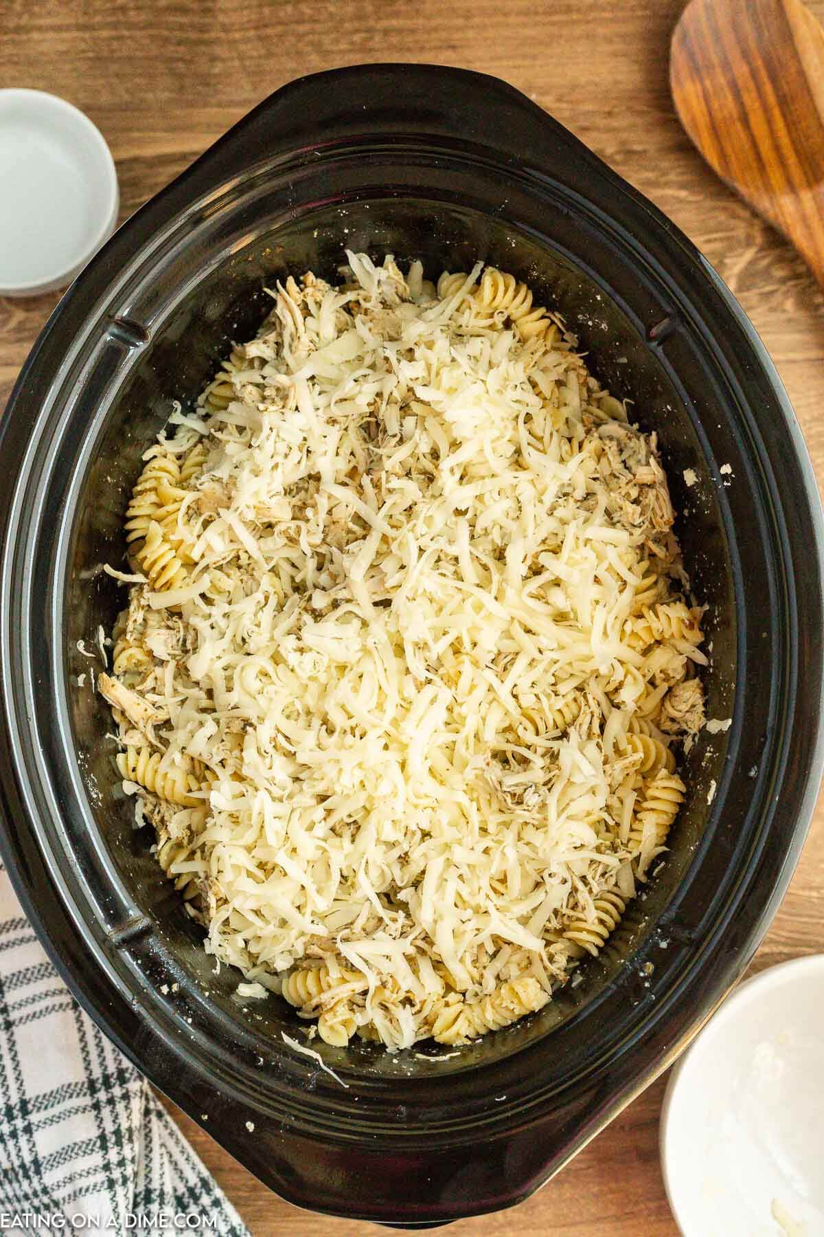 Topping the pesto chicken mixture with shredded cheese