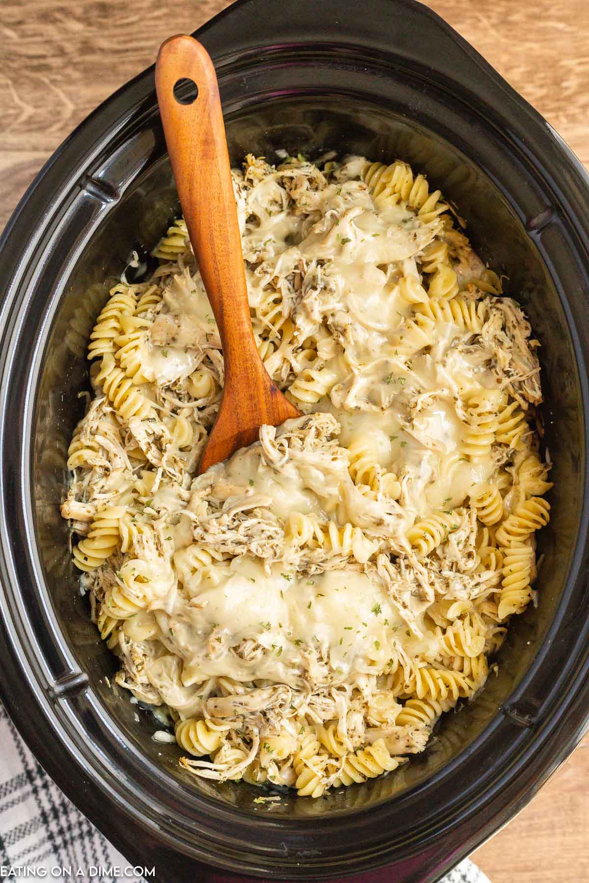 Pesto Chicken Pasta Casserole in the slow cooker with a wooden spoon