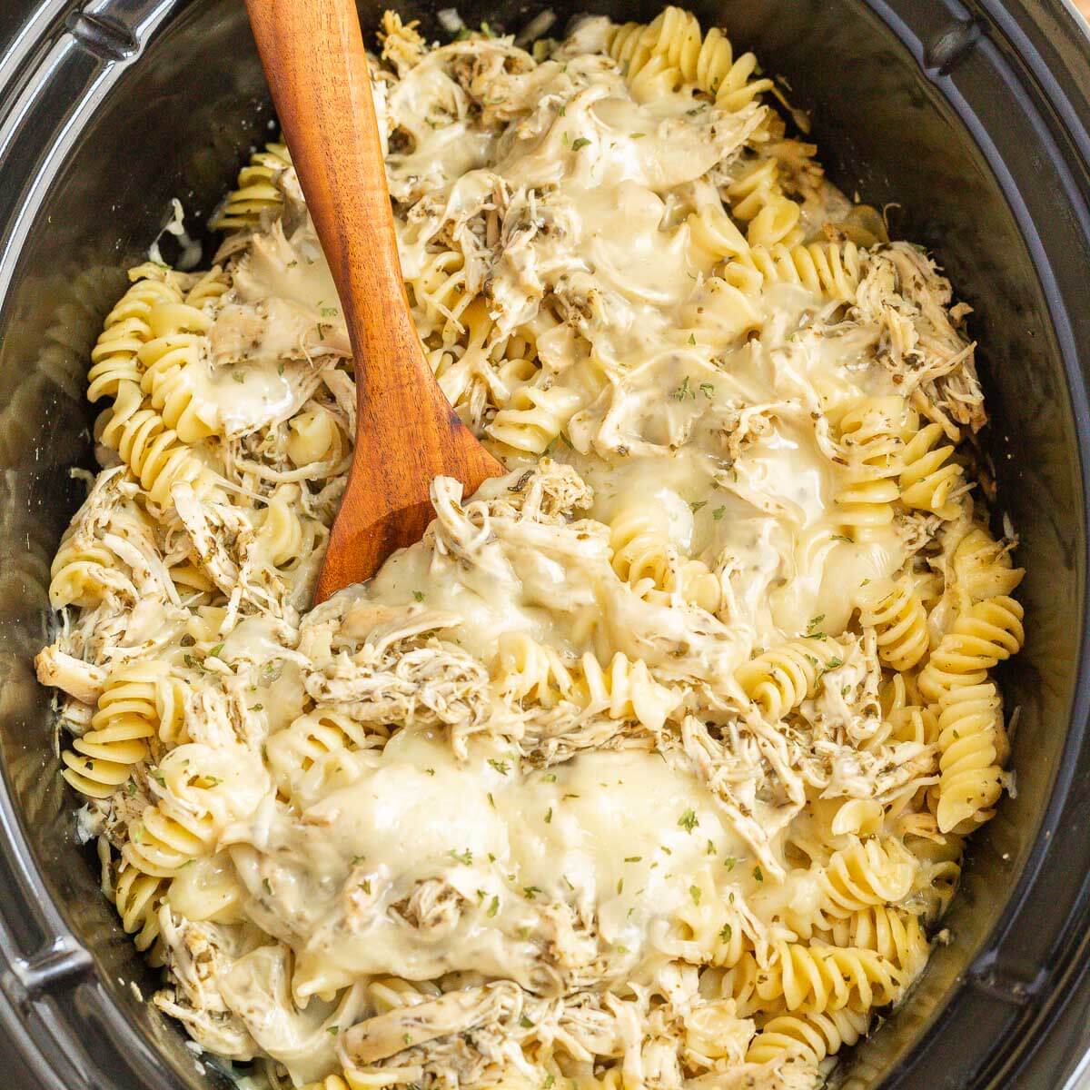 Close up image of pesto chicken pasta casserole in the slow cooker with a wooden spoon