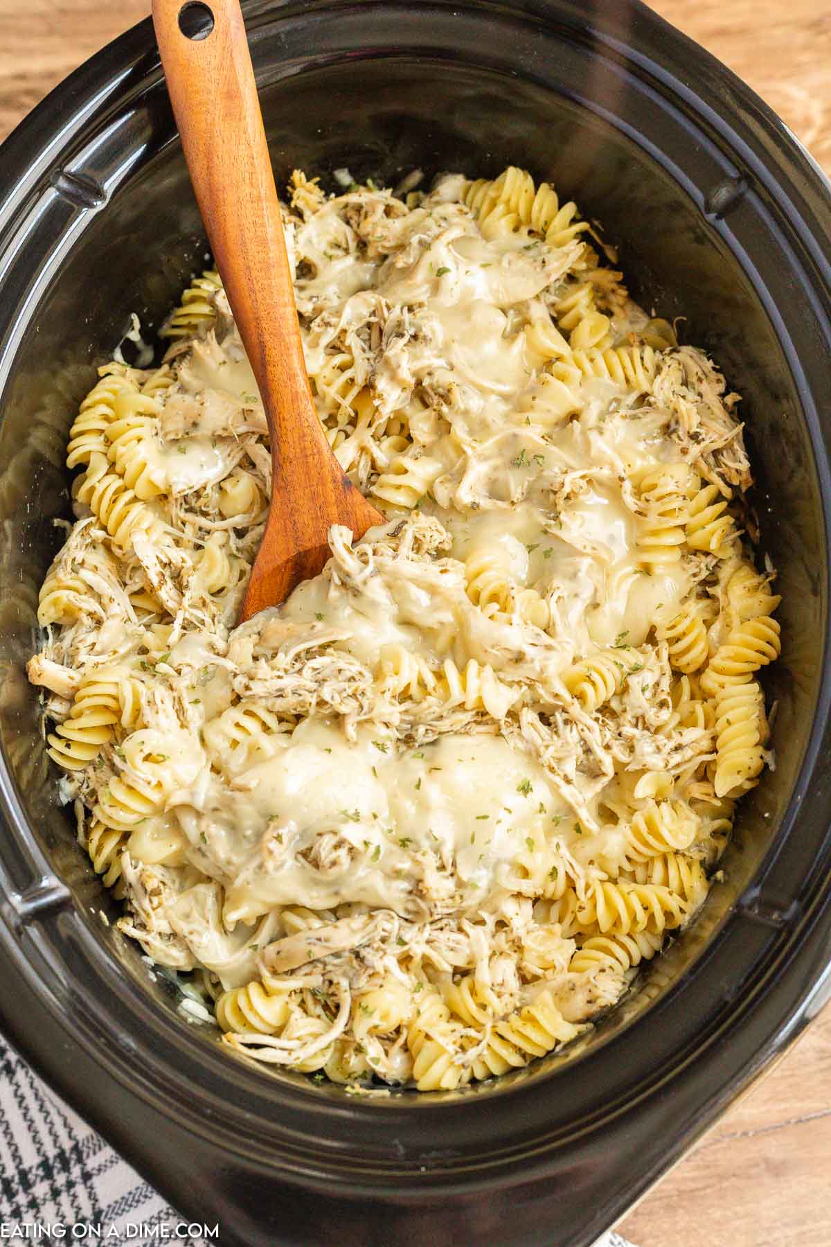 Pesto Chicken Pasta Casserole in the slow cooker with a wooden spoon