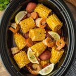 A Crock Pot Shrimp Boil featuring shrimp, corn on the cob pieces, red potatoes, sausage slices, and lemon wedges, all perfectly seasoned and slow-cooked together.