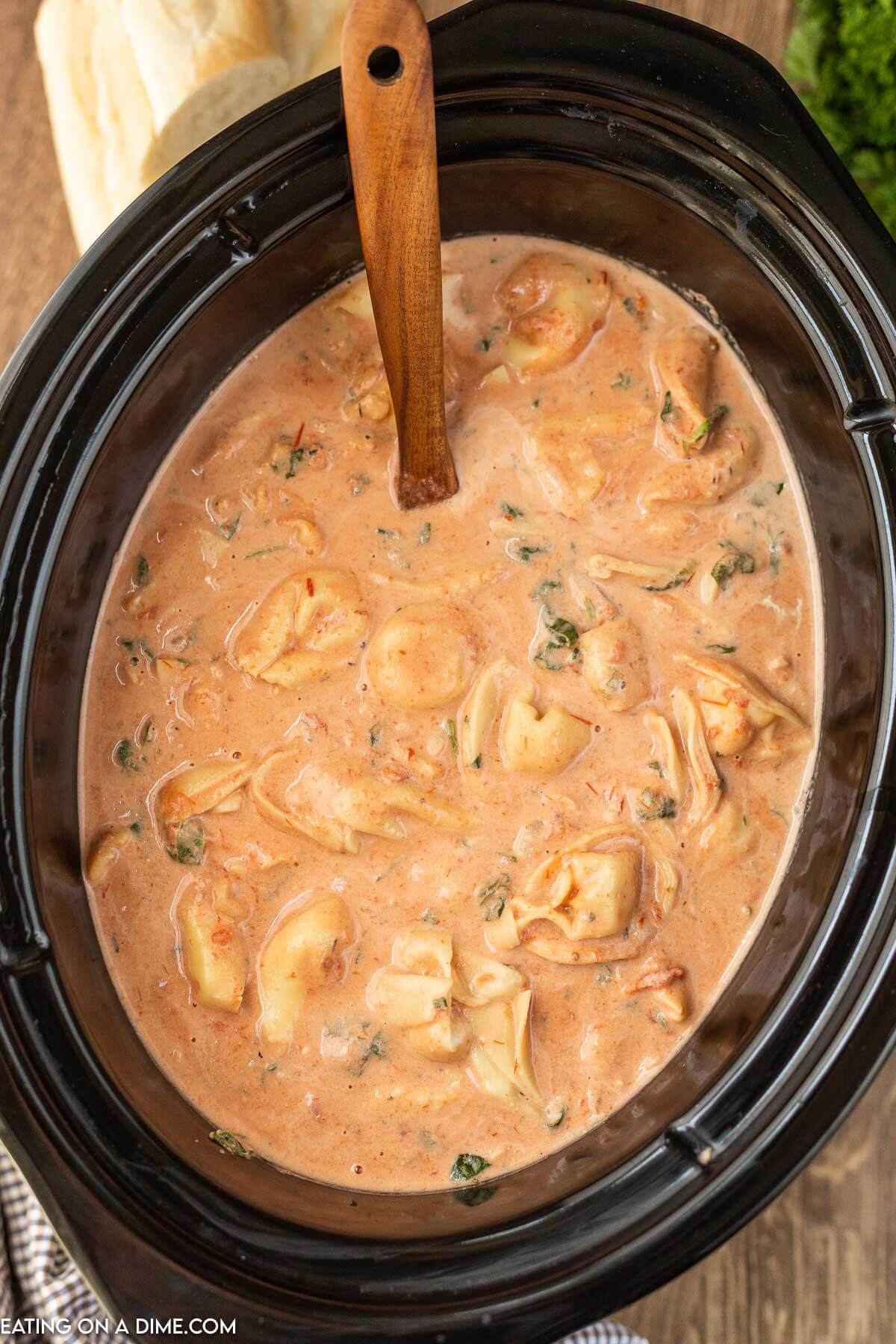Crockpot with spinach tortellini soup with a wooden spoon