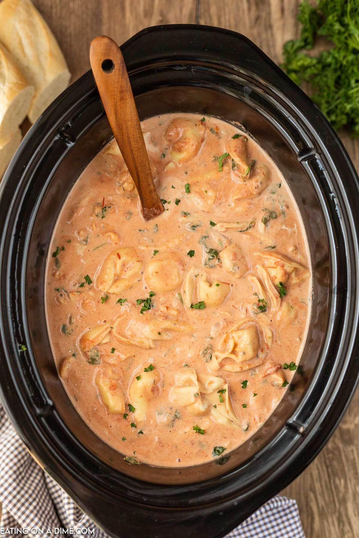 Crockpot with spinach tortellini soup with a wooden spoon