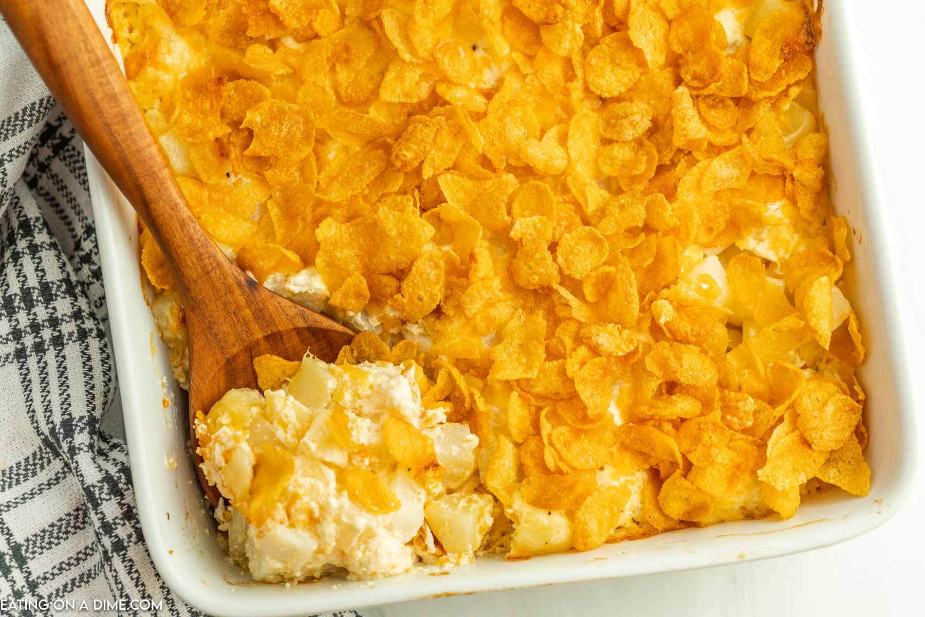 funeral potatoes in a casserole dish with a wooden spoon