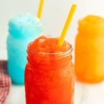 Three mason jars filled with colorful Sonic Slushie drinks—red, blue, and orange—each with a yellow straw. The frosty texture of these icy slushies pops against the light surface.