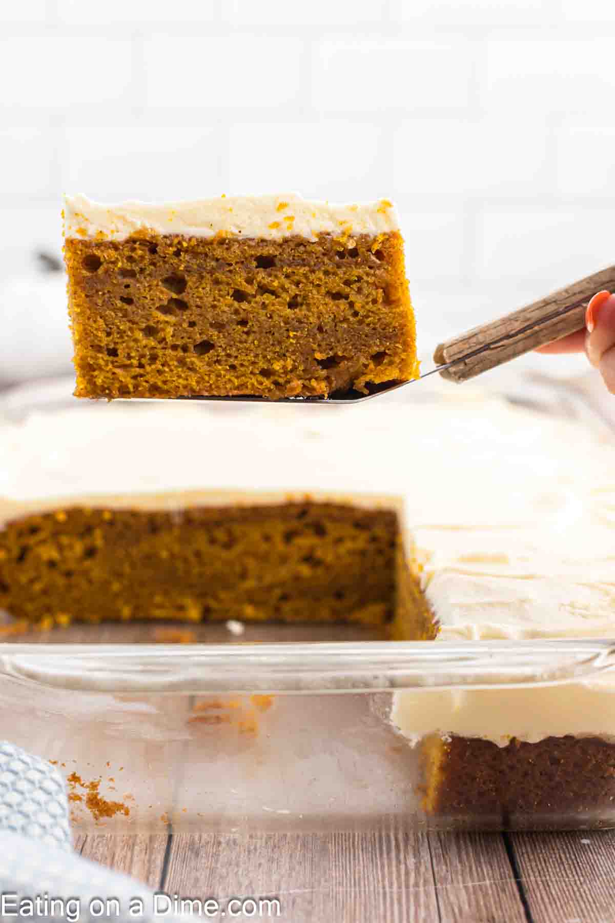 Pumpkin Cake with cream cheese frosting in a baking dish with a serving on a spatula