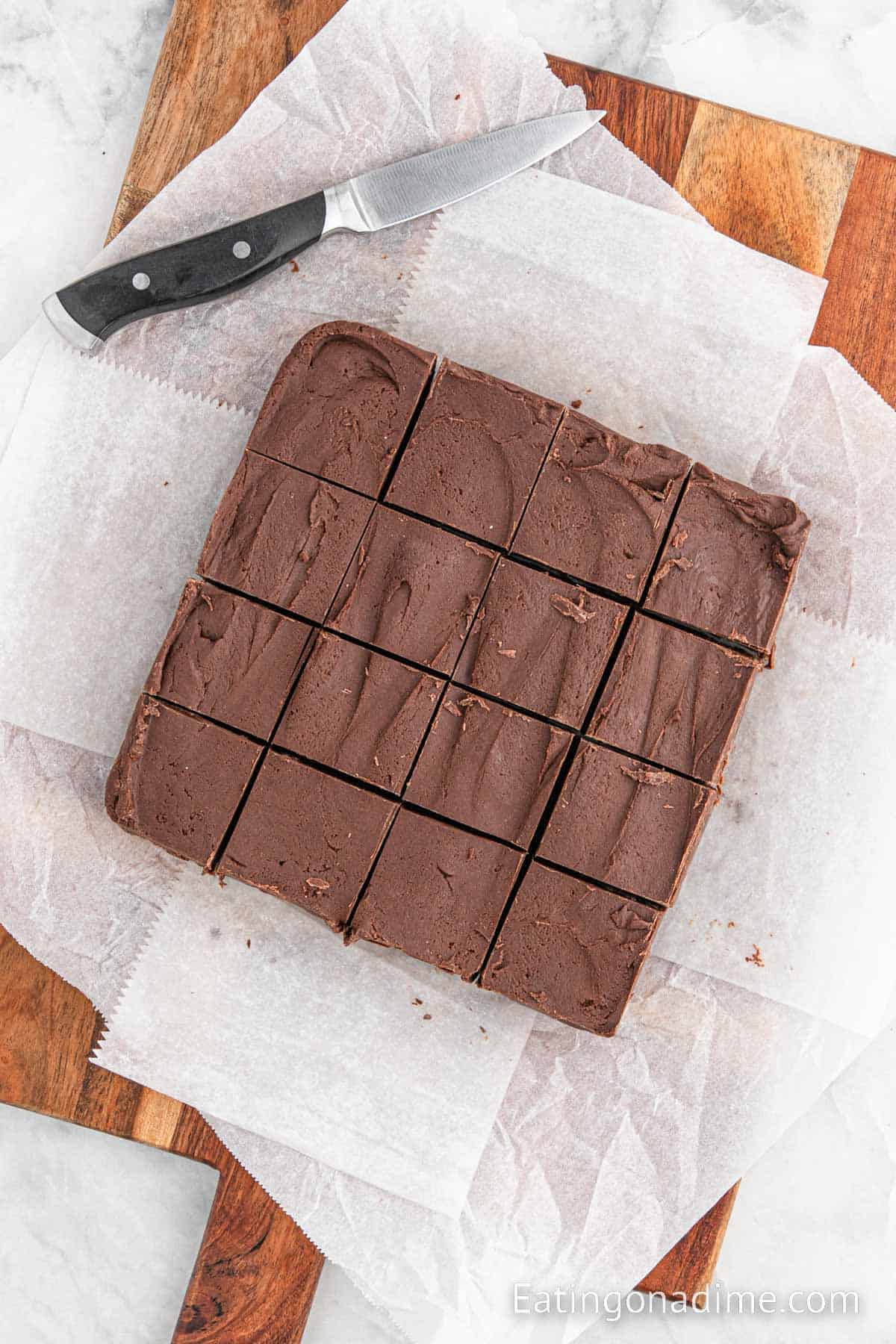 Chocolate fudge cut into squares on a cutting board with parchment paper
