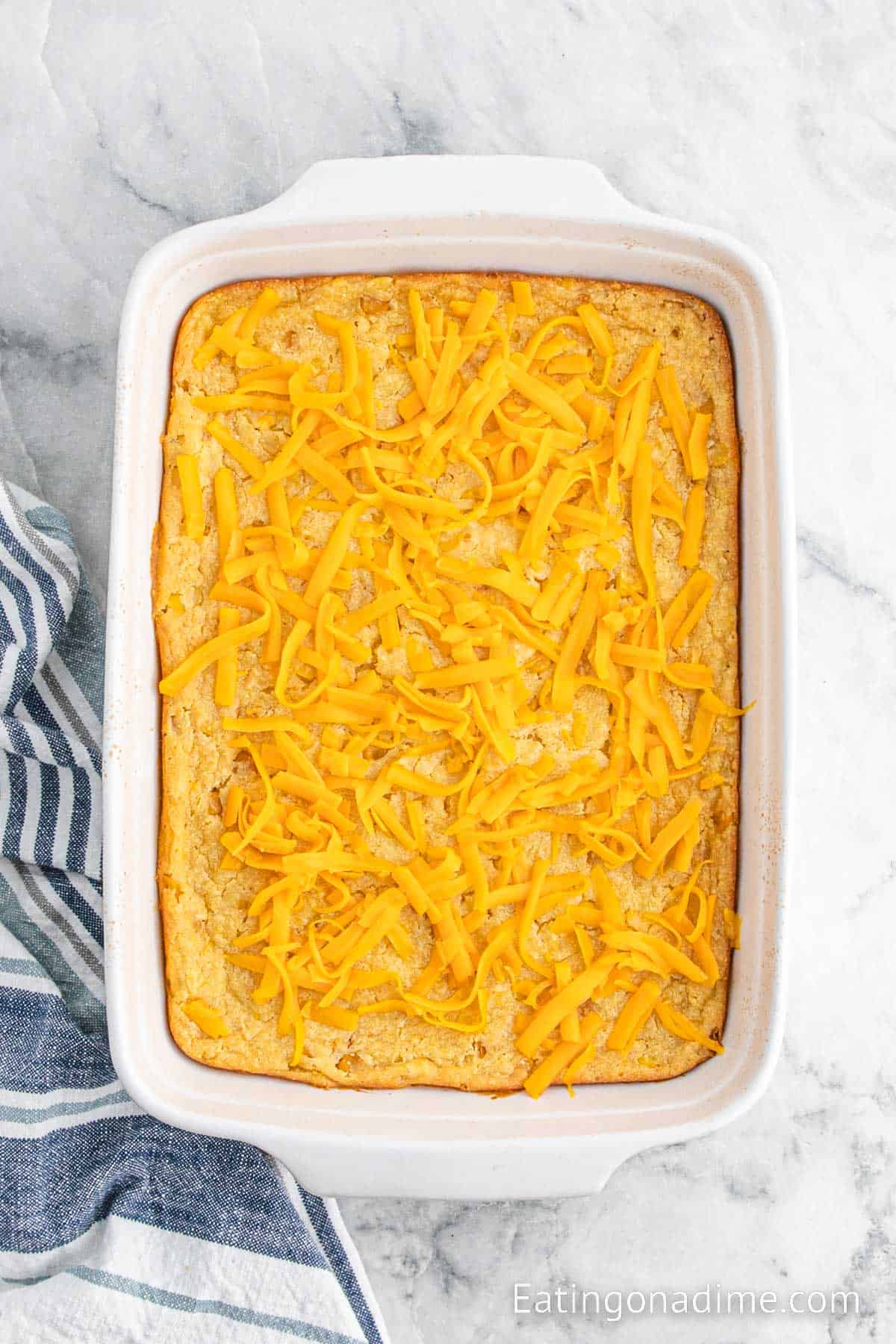 Baked corn casserole topped with shredded cheese in a baking dish