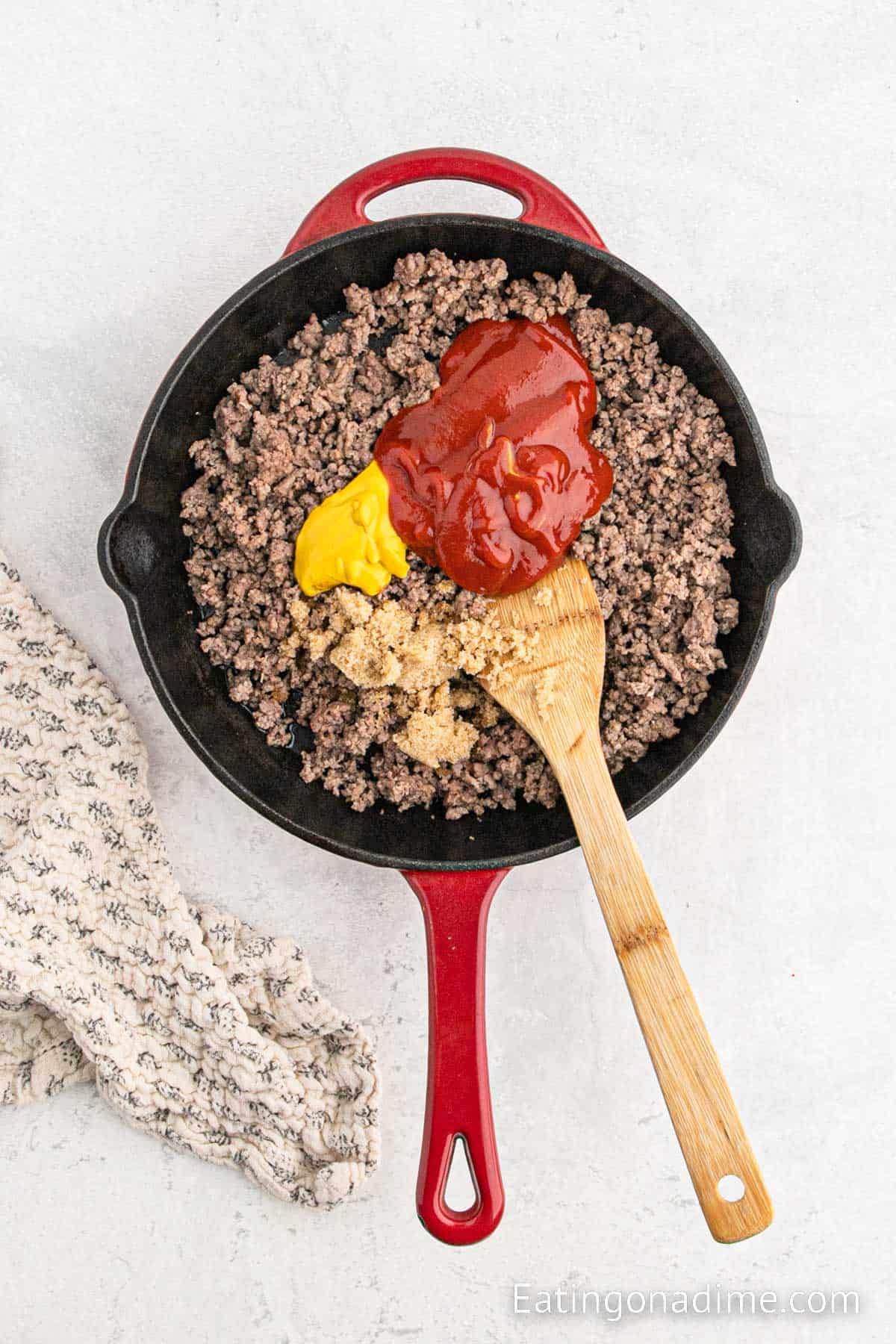 Adding in the ketchup, mustard and brown sugar in the skillet with a wooden spoon