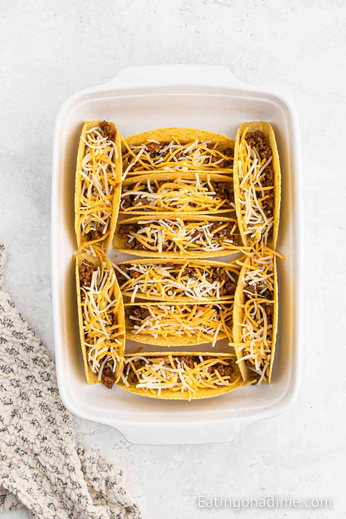Placing filled taco shells in a baking dish topped with cheese