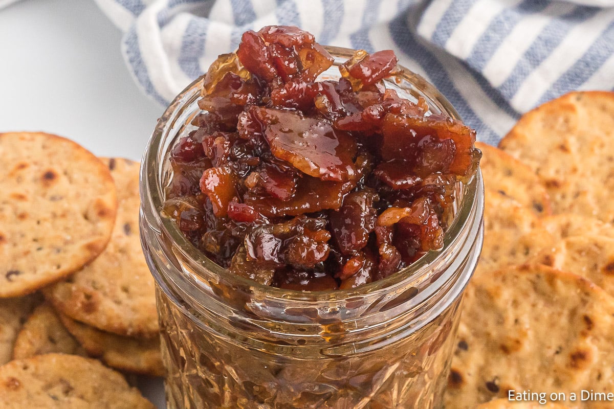 Bacon Jam in a jar with round crackers on the side.