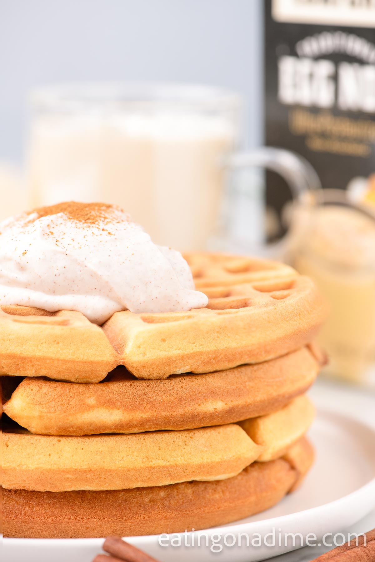 Stack of eggnog waffles with whipped cream on a plate. 