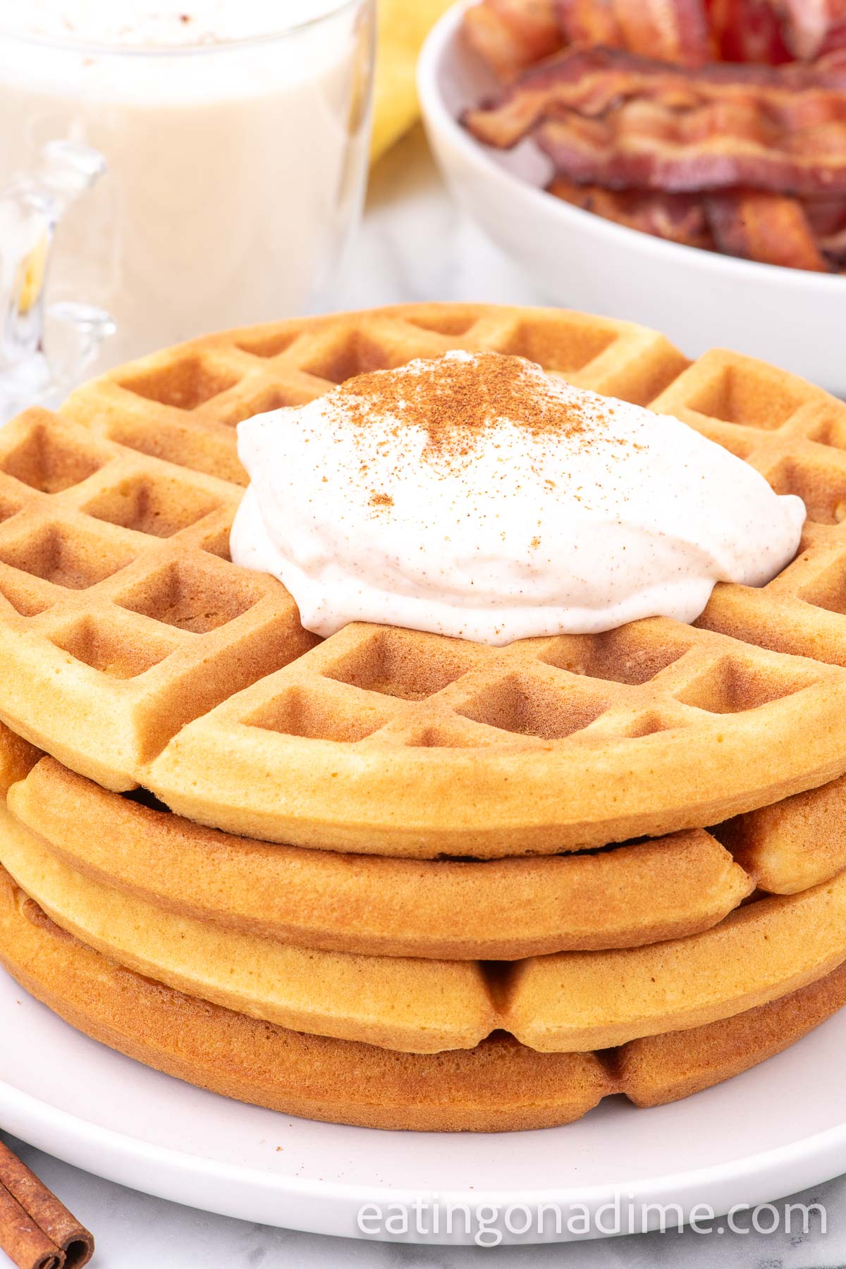 Stack of eggnog waffles with whipped cream on a plate. 