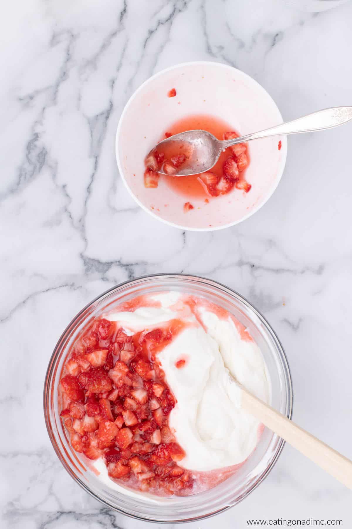 Chopped strawberries have been added to the cream mixture in a bowl.