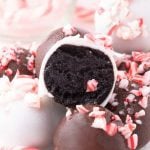 Close-up of chocolate truffles coated in white and dark chocolate, topped with crushed peppermint candy. Inspired by Peppermint Oreo balls Recipe, these festive treats are colorful and perfect for the holidays. One is cut open to reveal its rich interior.
