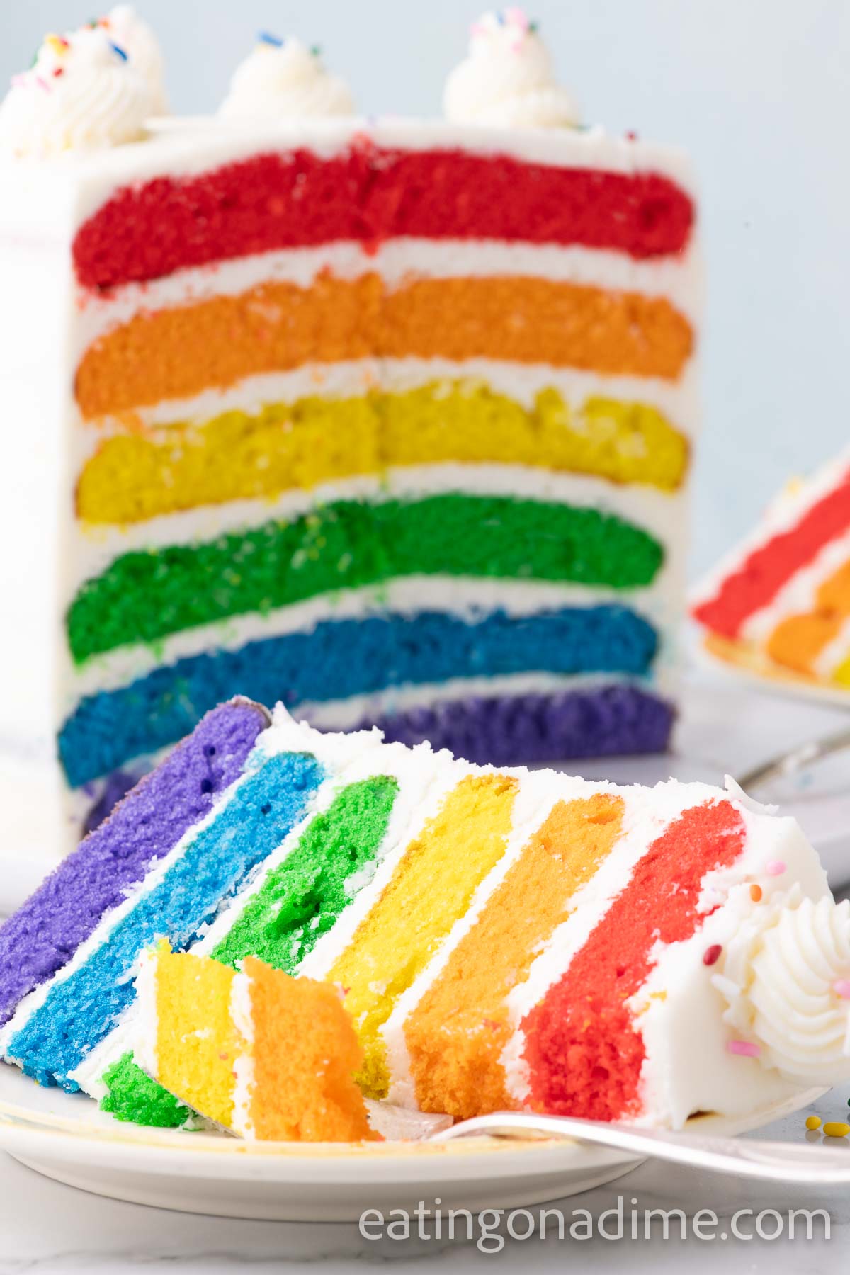 Close up image of a slice of frosted Rainbow Cake