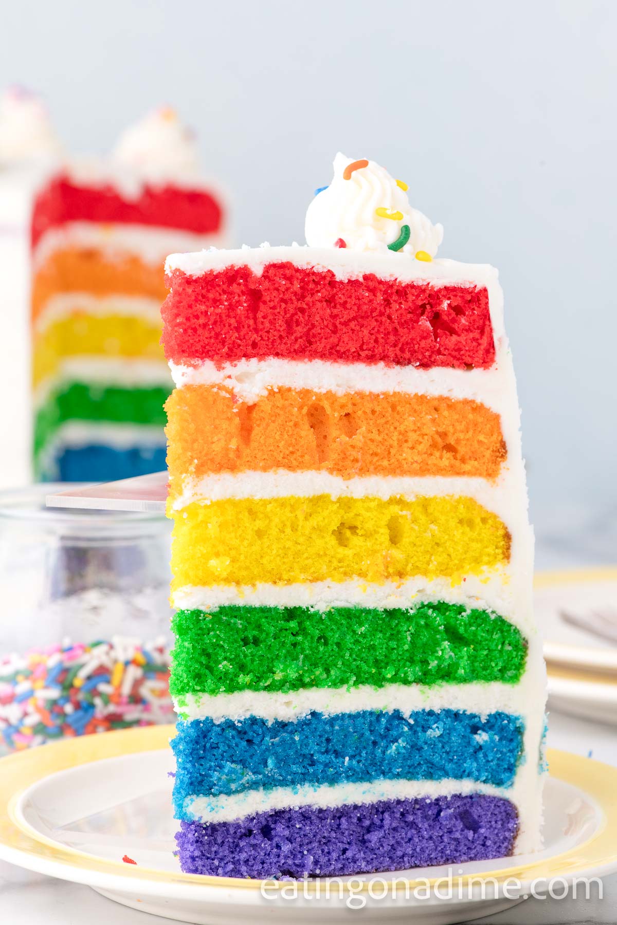 Close up image of a slice of frosted Rainbow Cake
