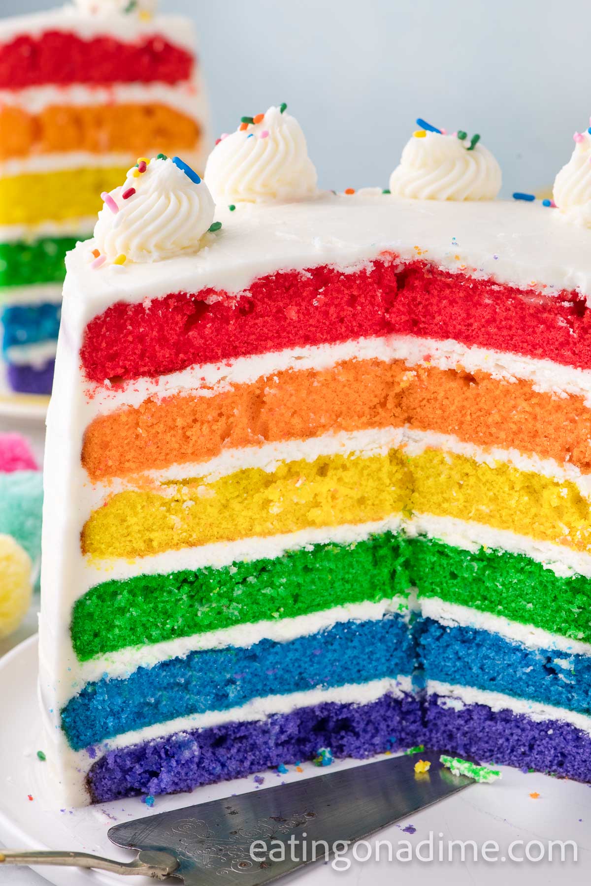 Close up image of frosted Rainbow Cake sliced to see all the rainbow layers
