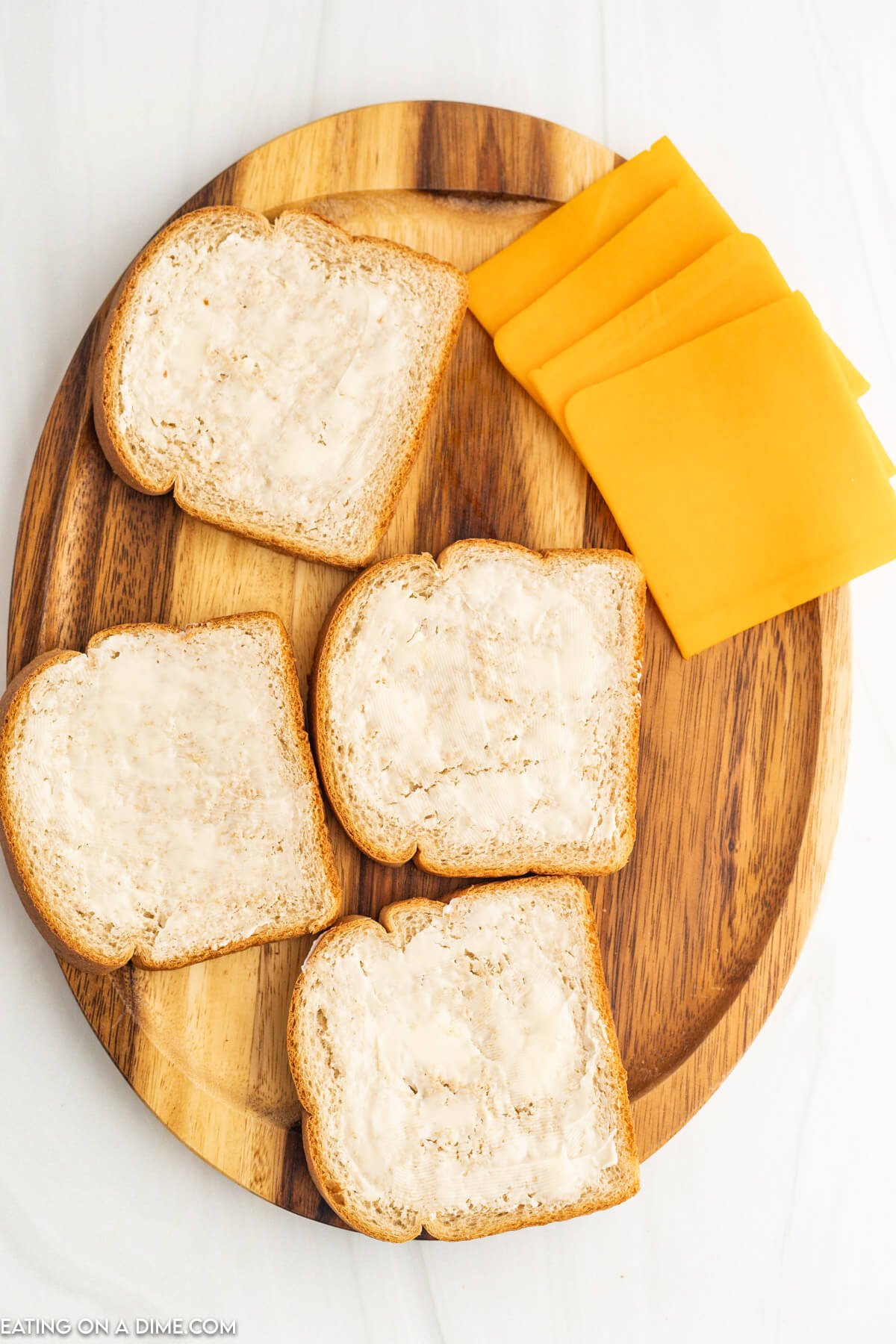 Butter spread on slices of bread and slices of cheese on a cutting board