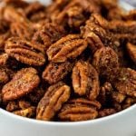 A close-up of a white bowl filled with Air Fryer Candied Pecans, roasted to perfection and coated in a brown, spiced seasoning. The pecans appear crunchy and flavorful.