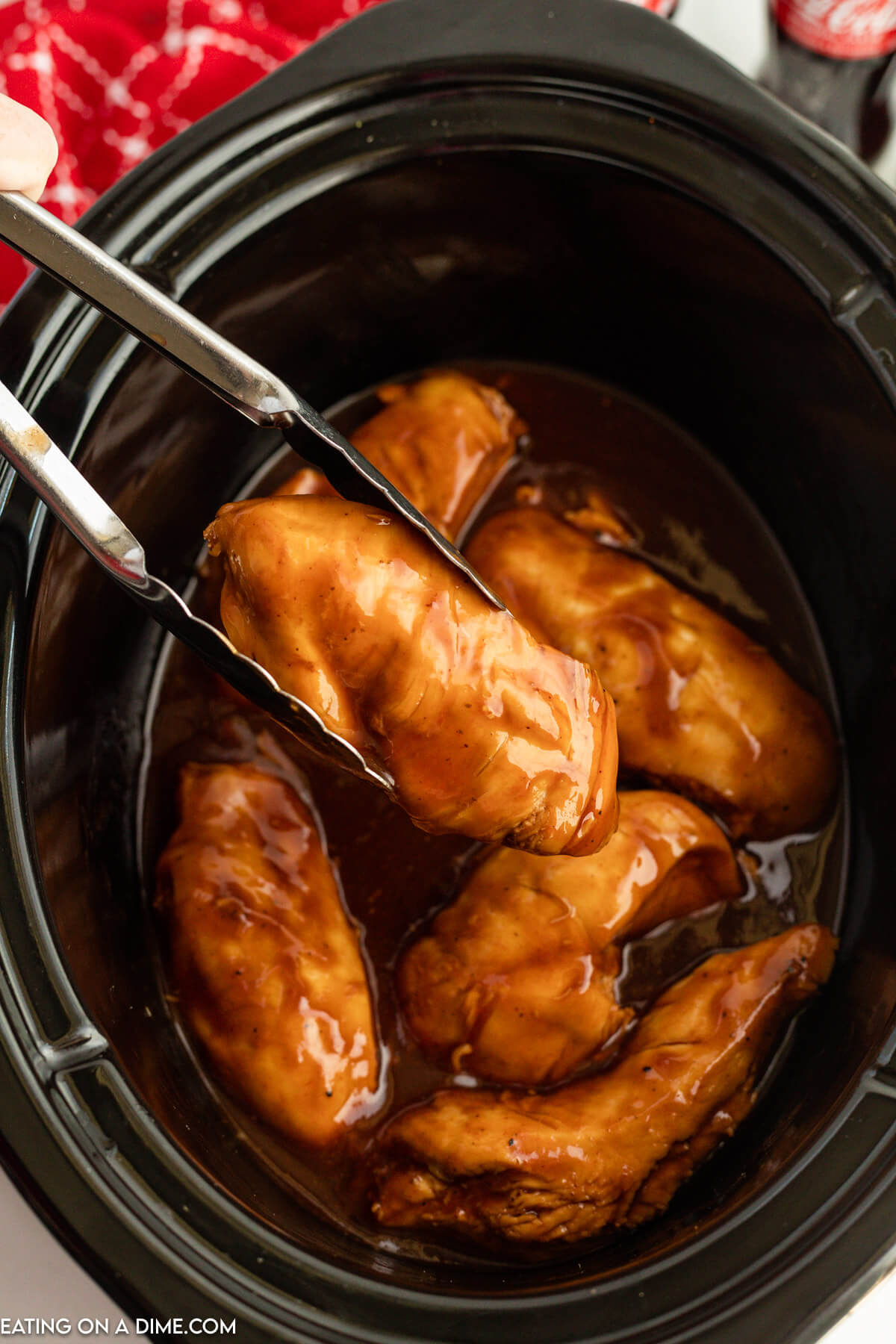 Cooked Coca Cola Chicken in the slow cooker with a piece on tongs