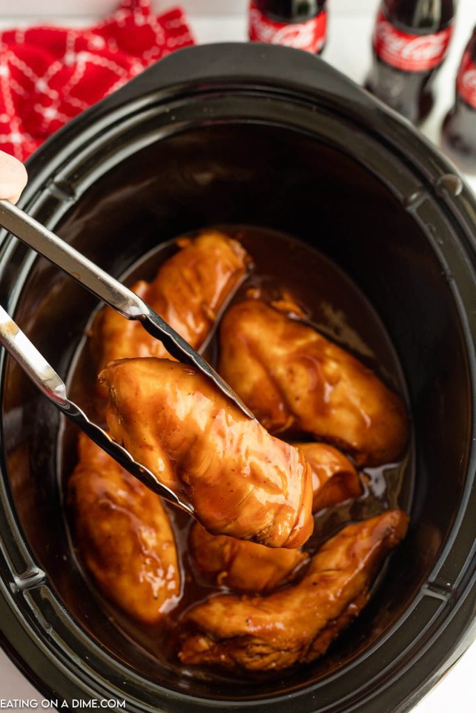Cooked Coca Cola Chicken in the slow cooker with a piece on tongs