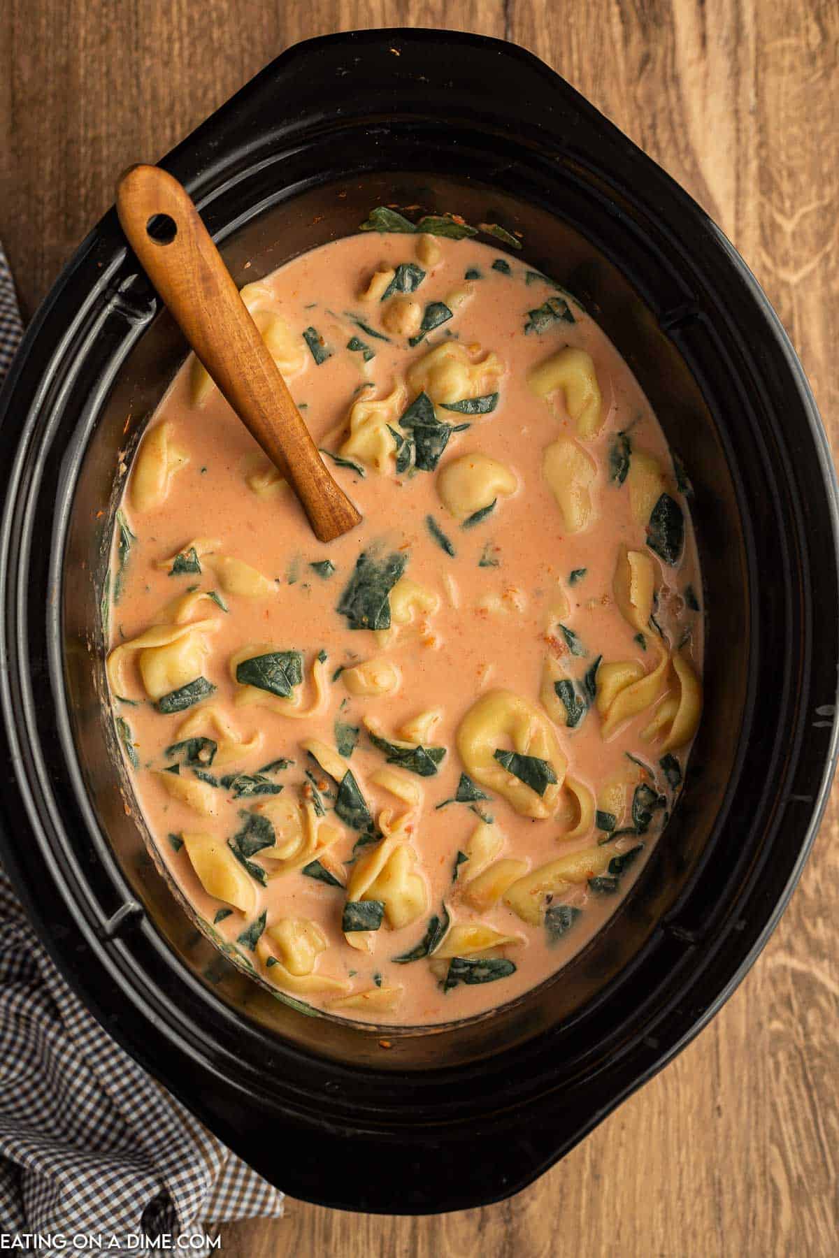 Cooked tortellini soup in the slow cooker with a wooden spoon