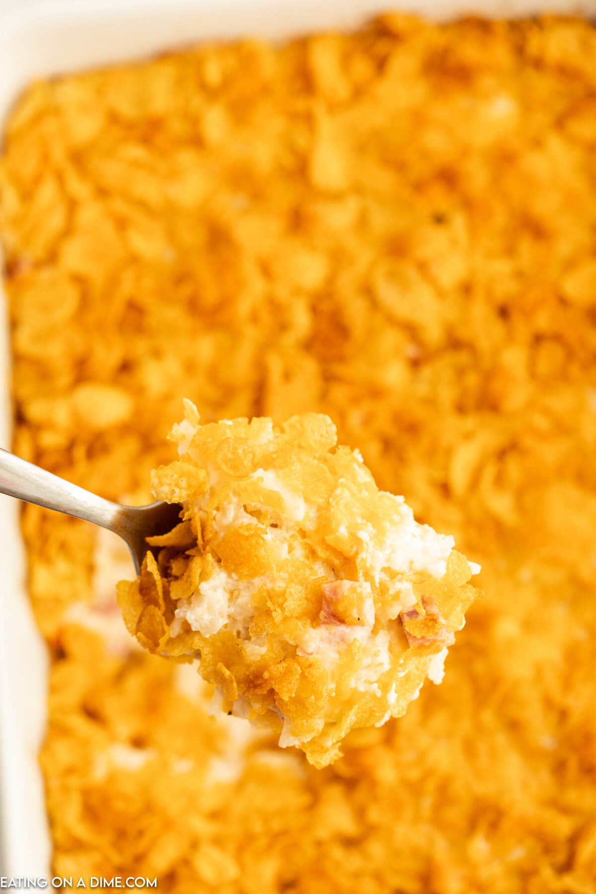 Funeral potatoes in a baking dish with a serving on a spoon