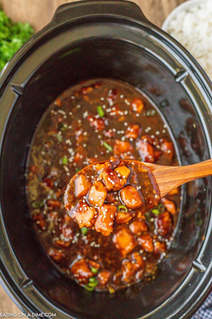 Orange chicken in a slow cooker with a serving on a wooden spoon