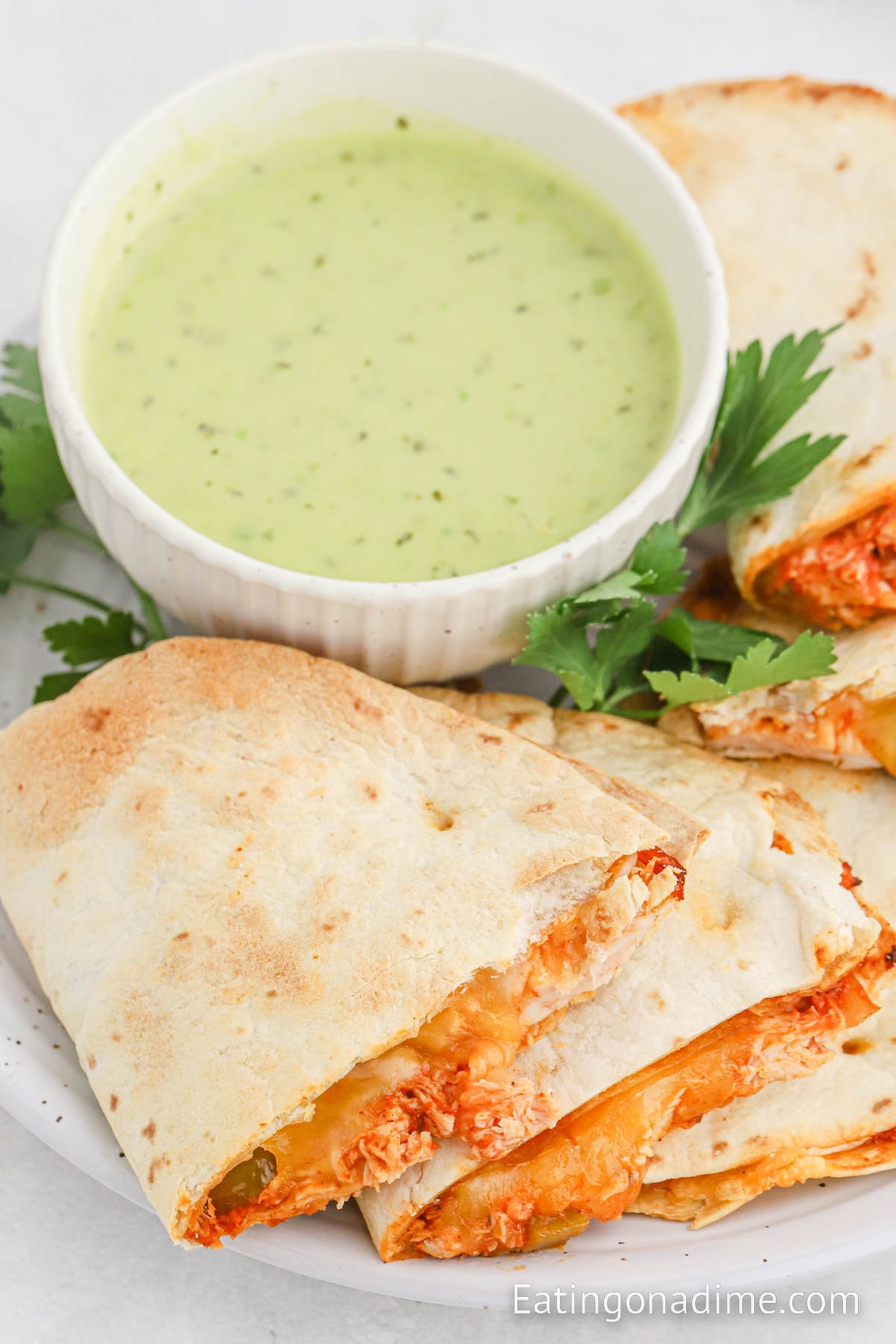 Chicken quesadillas stacked on a plate with a side of green sauce