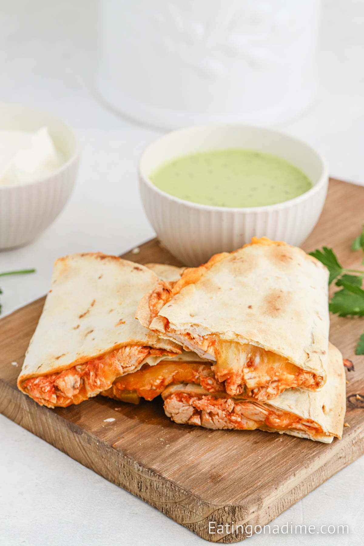 Chicken quesadillas stacked on a cutting board with a side of green sauce