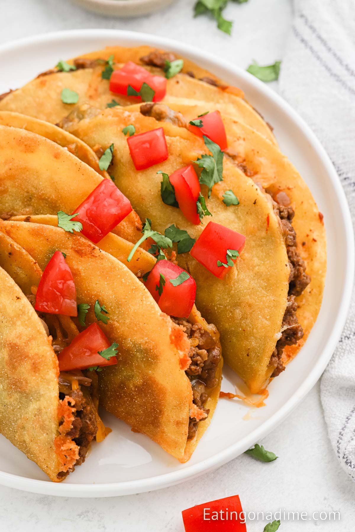 Fried tacos topped with cheese, tomatoes and fresh cilantro on a plate