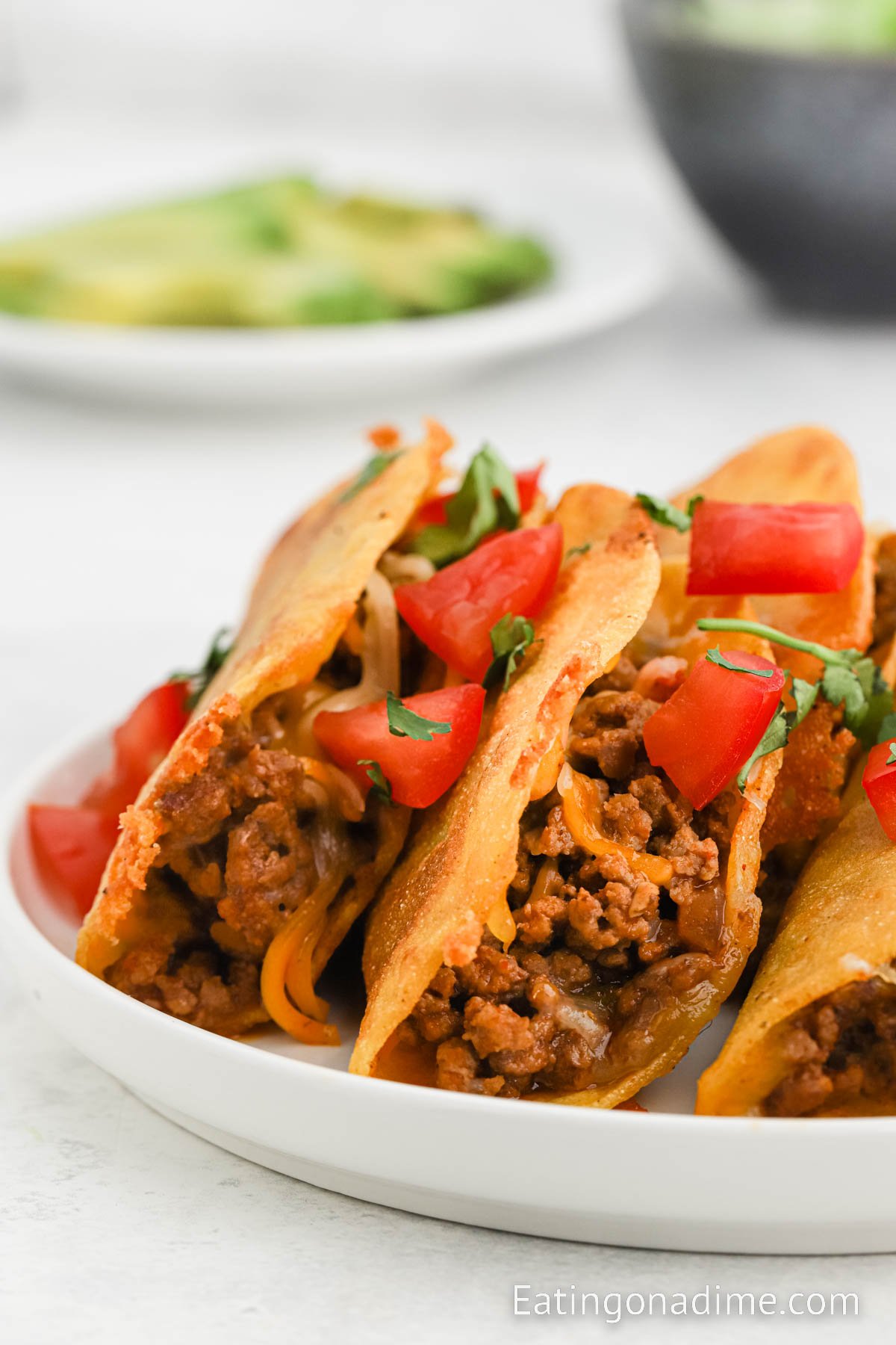 Fried tacos topped with cheese, tomatoes and fresh cilantro on a plate