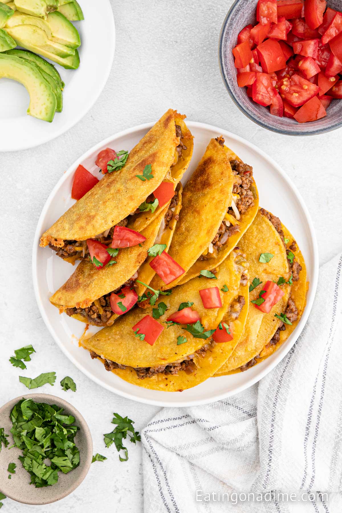 Fried tacos topped with cheese, tomatoes and fresh cilantro on a plate