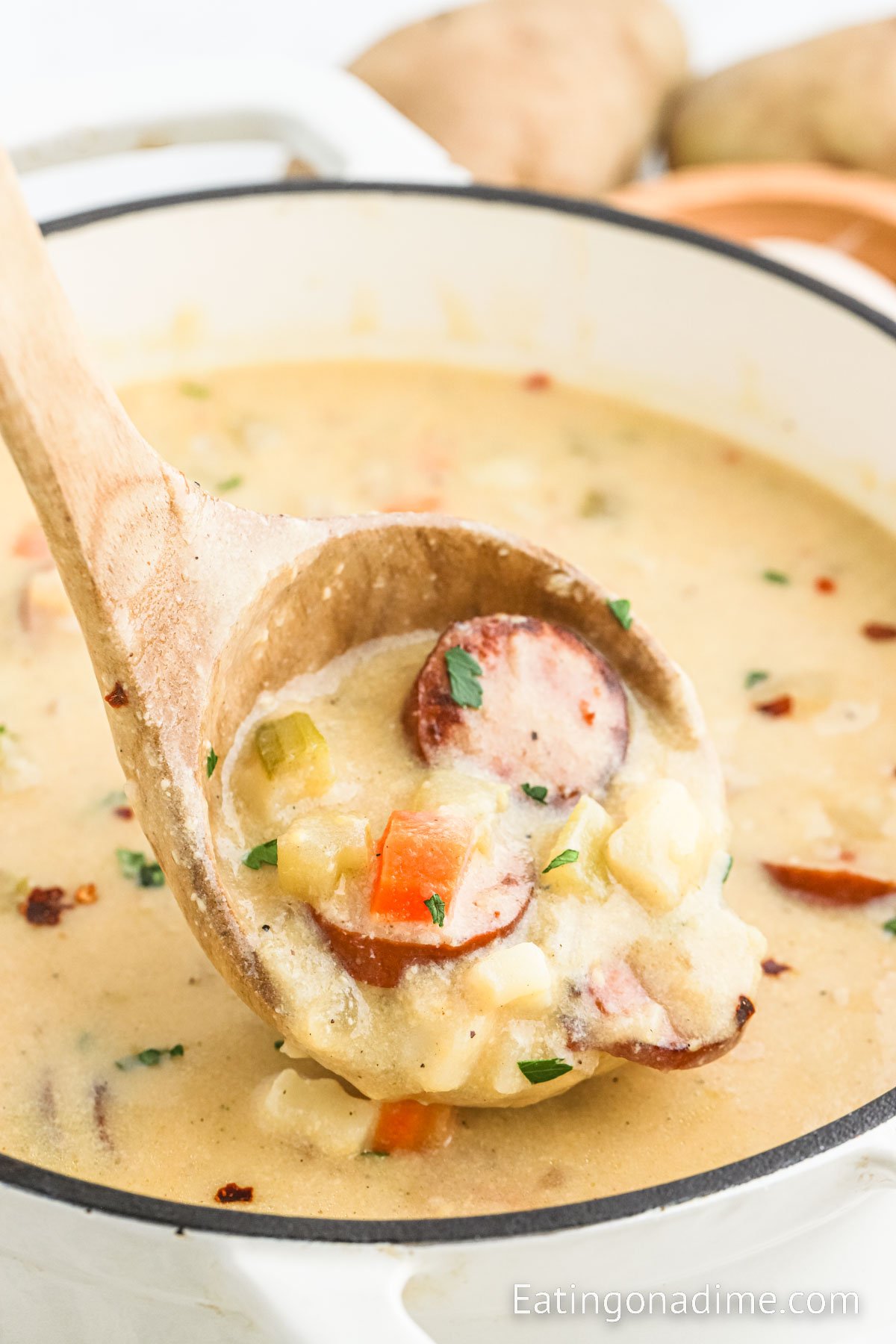 Potato Kielbasa Soup in a large pot with a serving on a wooden spoon