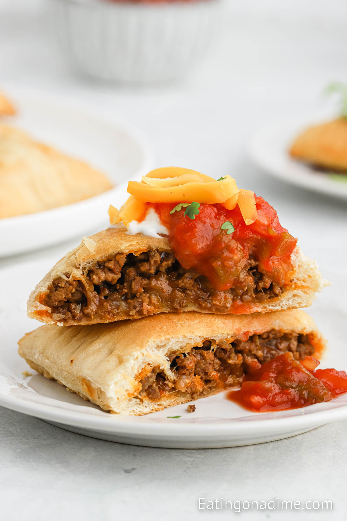 Taco Pockets stacked on a plate and topped with cheese, salsa and sour cream