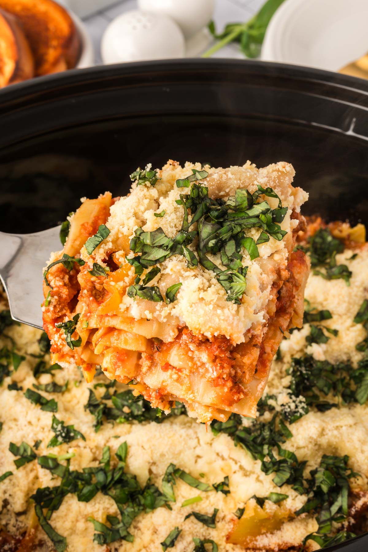 Lasagna in the crock pot with a close up image of a serving on a spatula