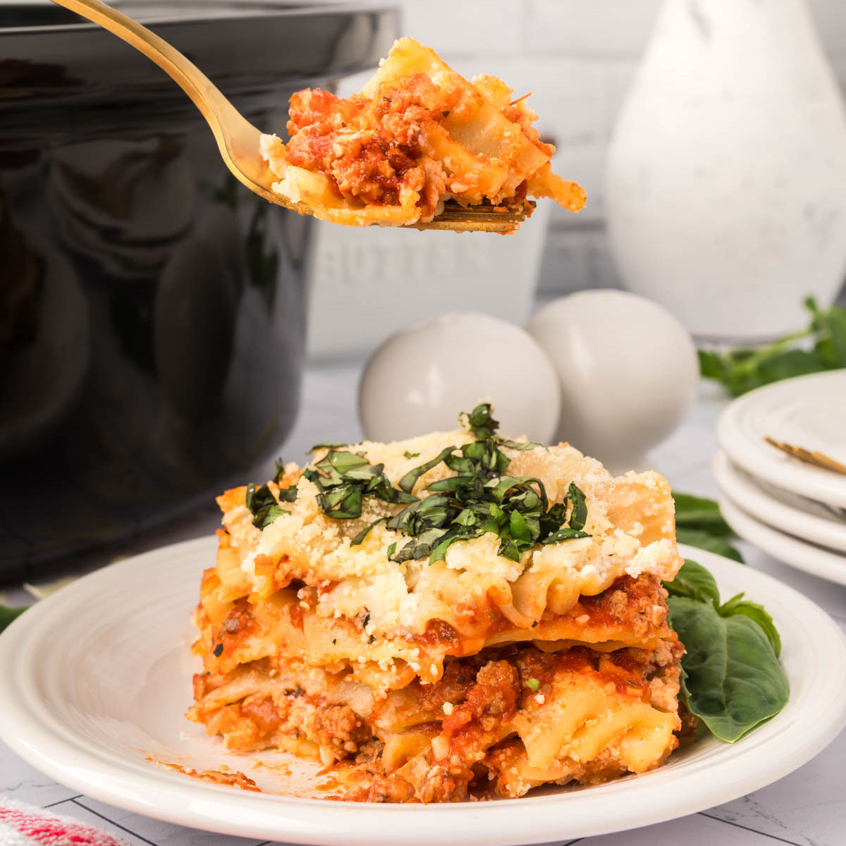 Serving of lasagna on a white plate with a bite on a fork