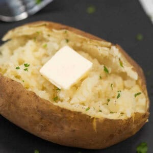 A baked potato on a black platter topped with pepper and butter.
