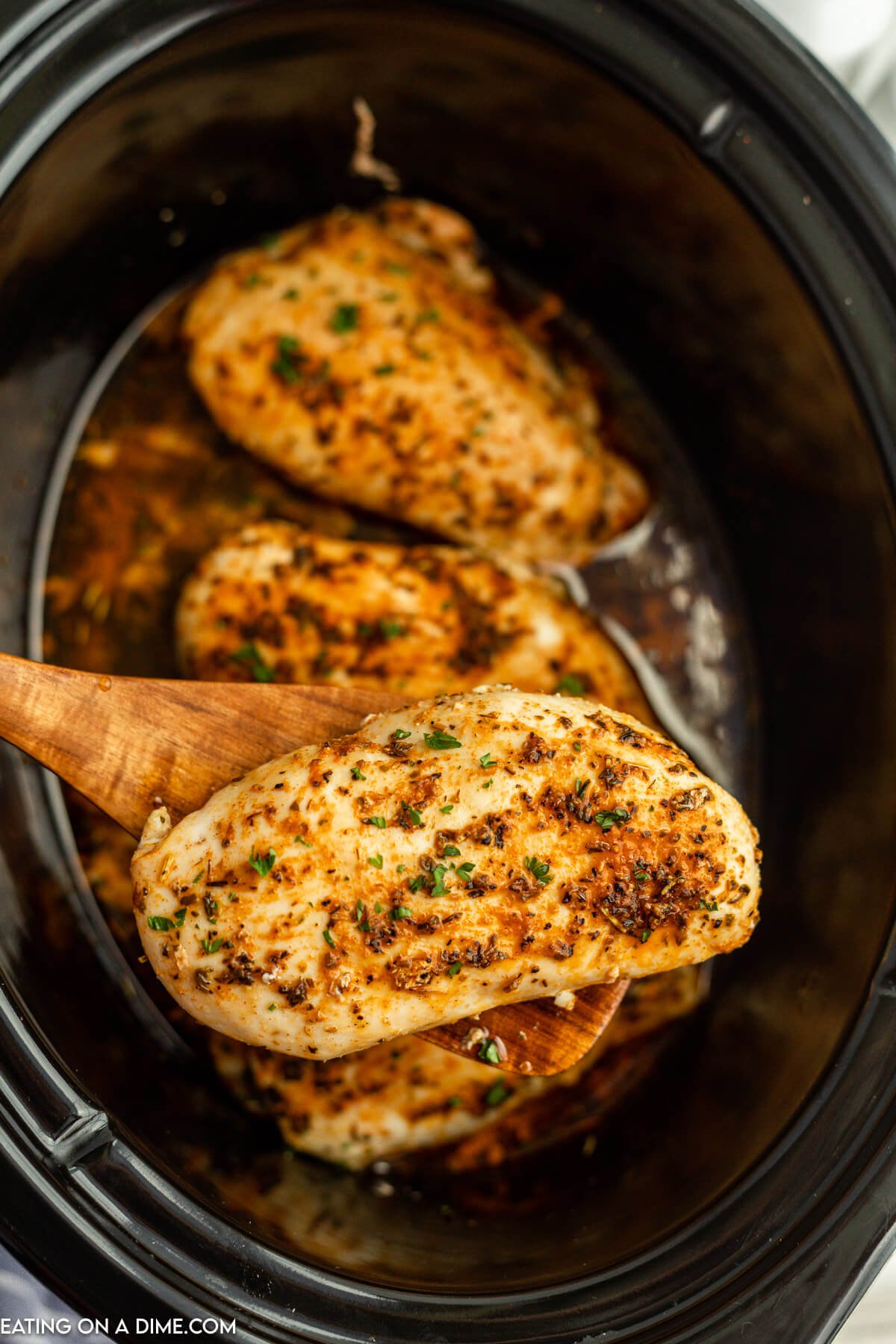 Cooked Chicken Breast in the slow cooker with a serving on a wooden spoon
