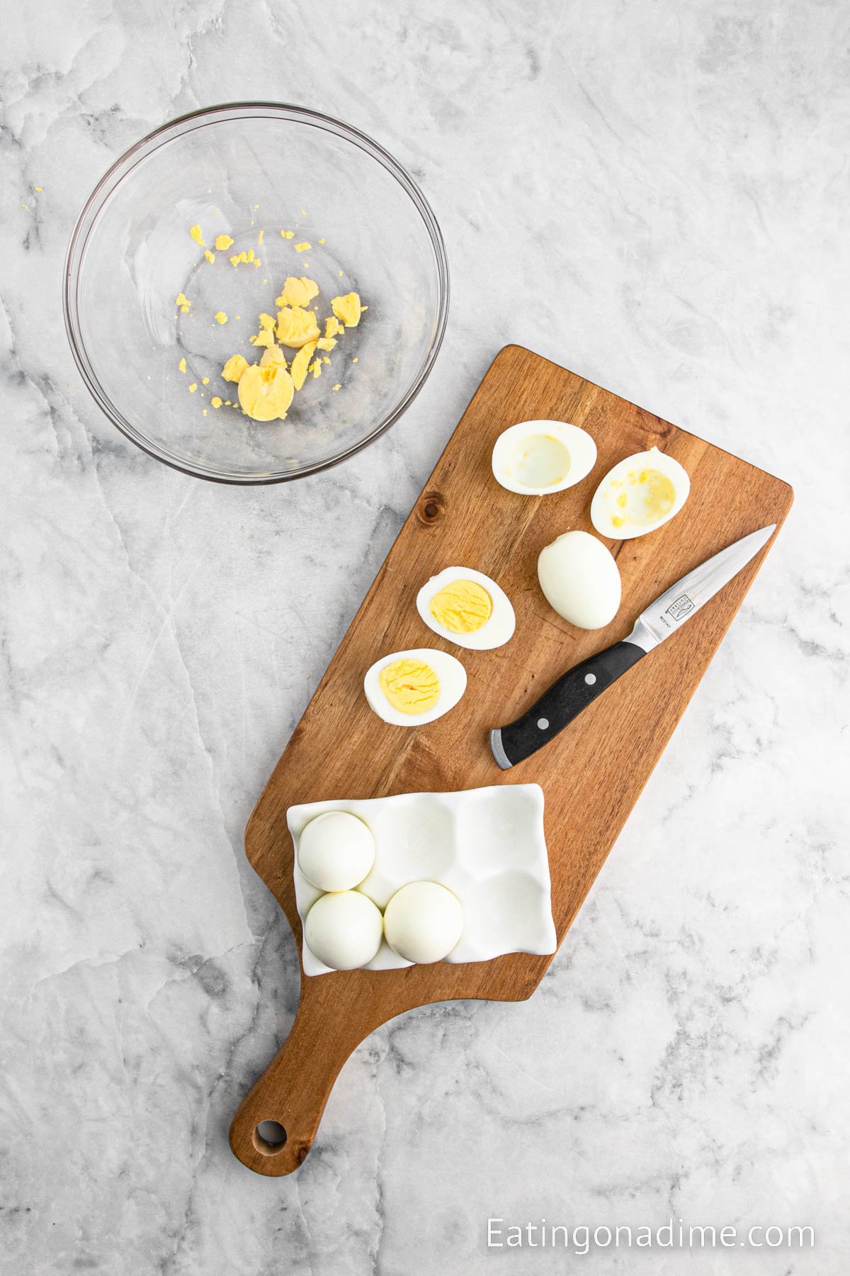 Hard boiled eggs cut in half on a cutting board with a knife and a bowl