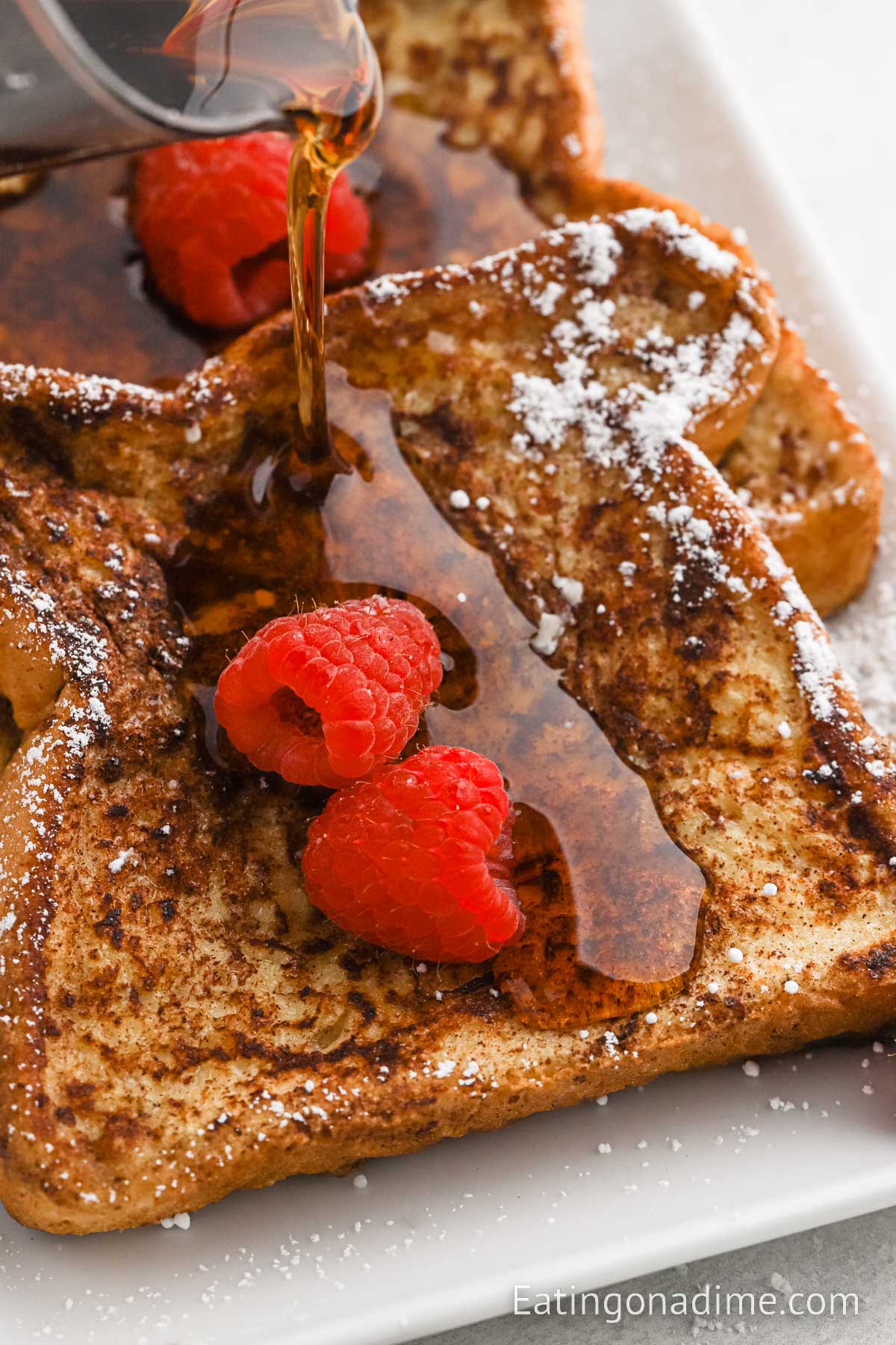 Syrup being poured over cinnamon french toast with fresh berries