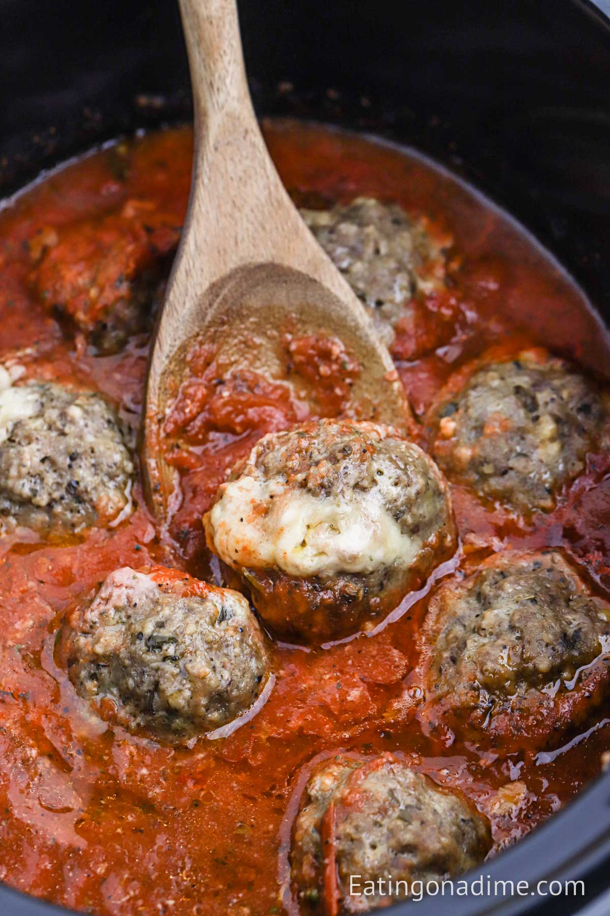 Mozzarella Stuffed Meatballs in the crock pot with sauce and a serving on a wooden spoon