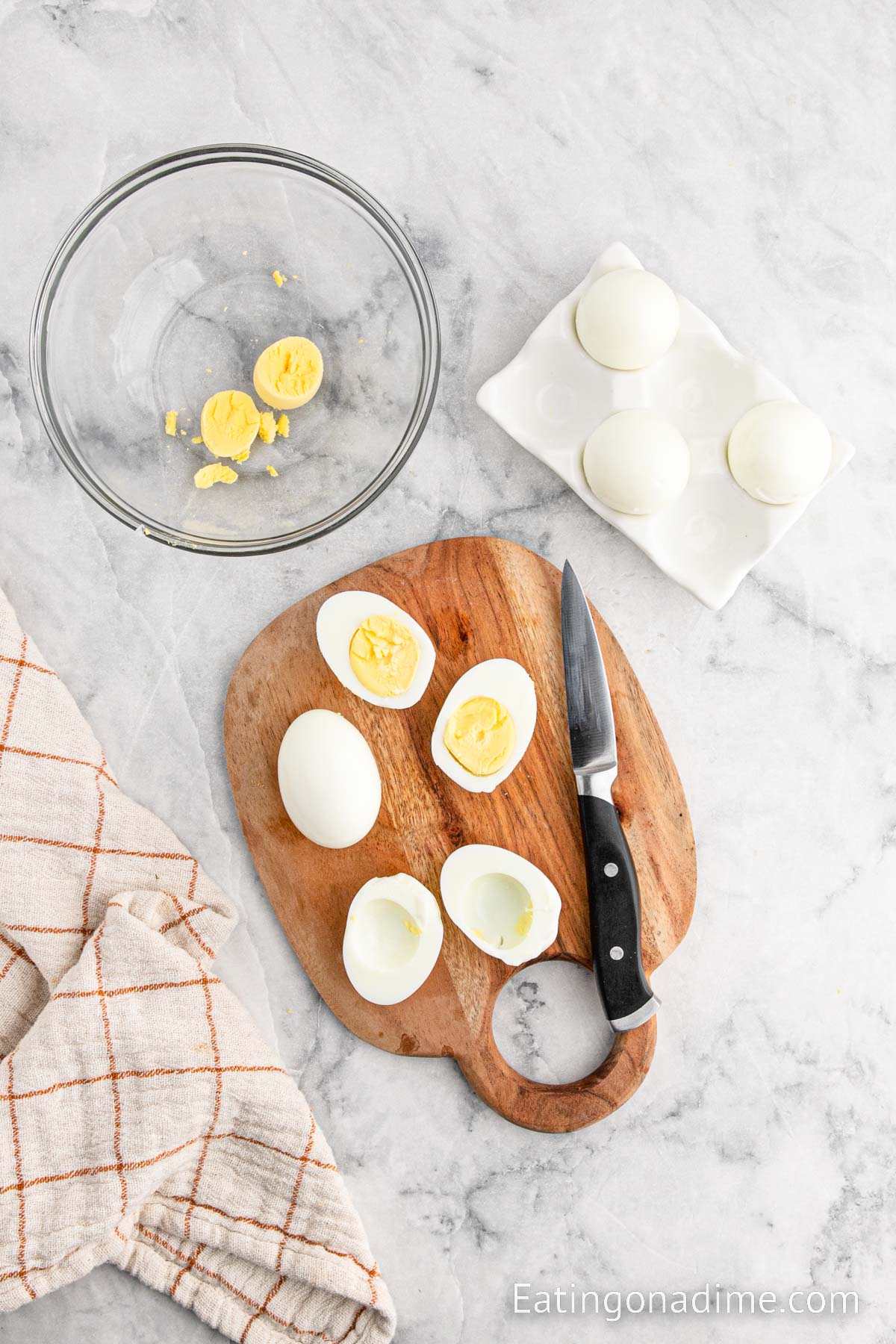 Slicing hard boiled eggs on a cutting board and placing yolk in the bowl
