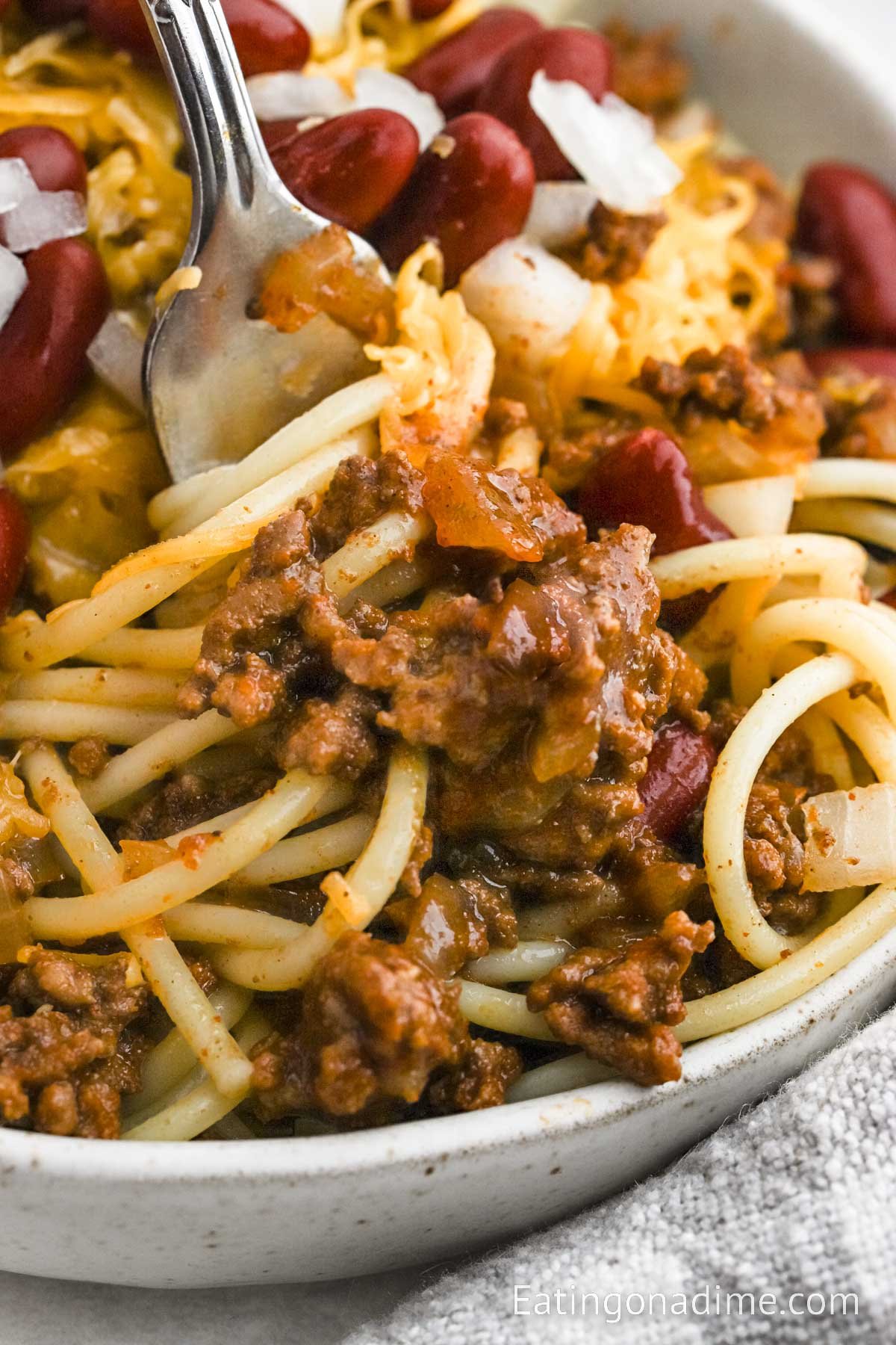 Close up image of Cincinnati Chili on cooked noodles in a bowl with a fork