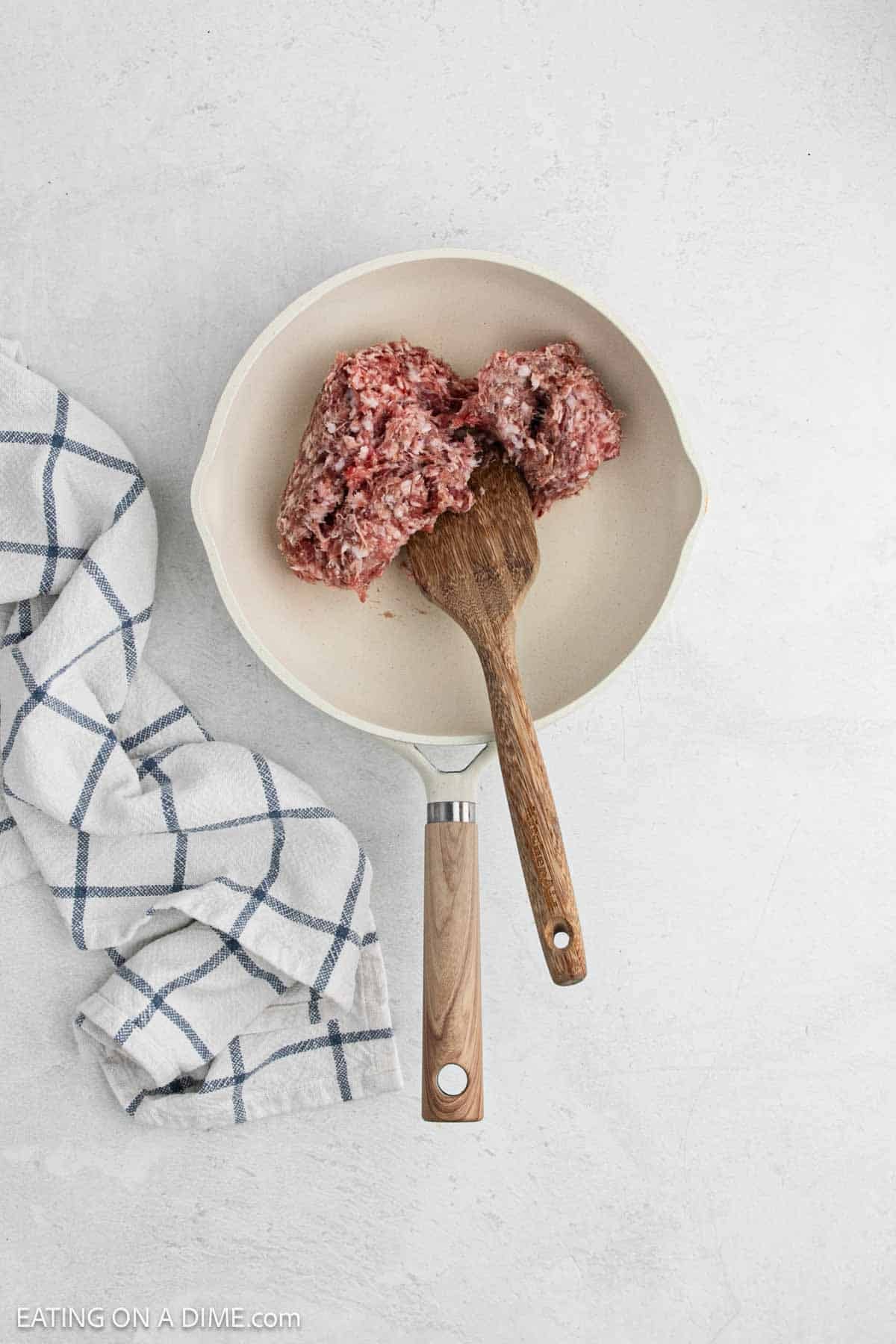 Cooking sausage in a skillet with a wooden spoon.